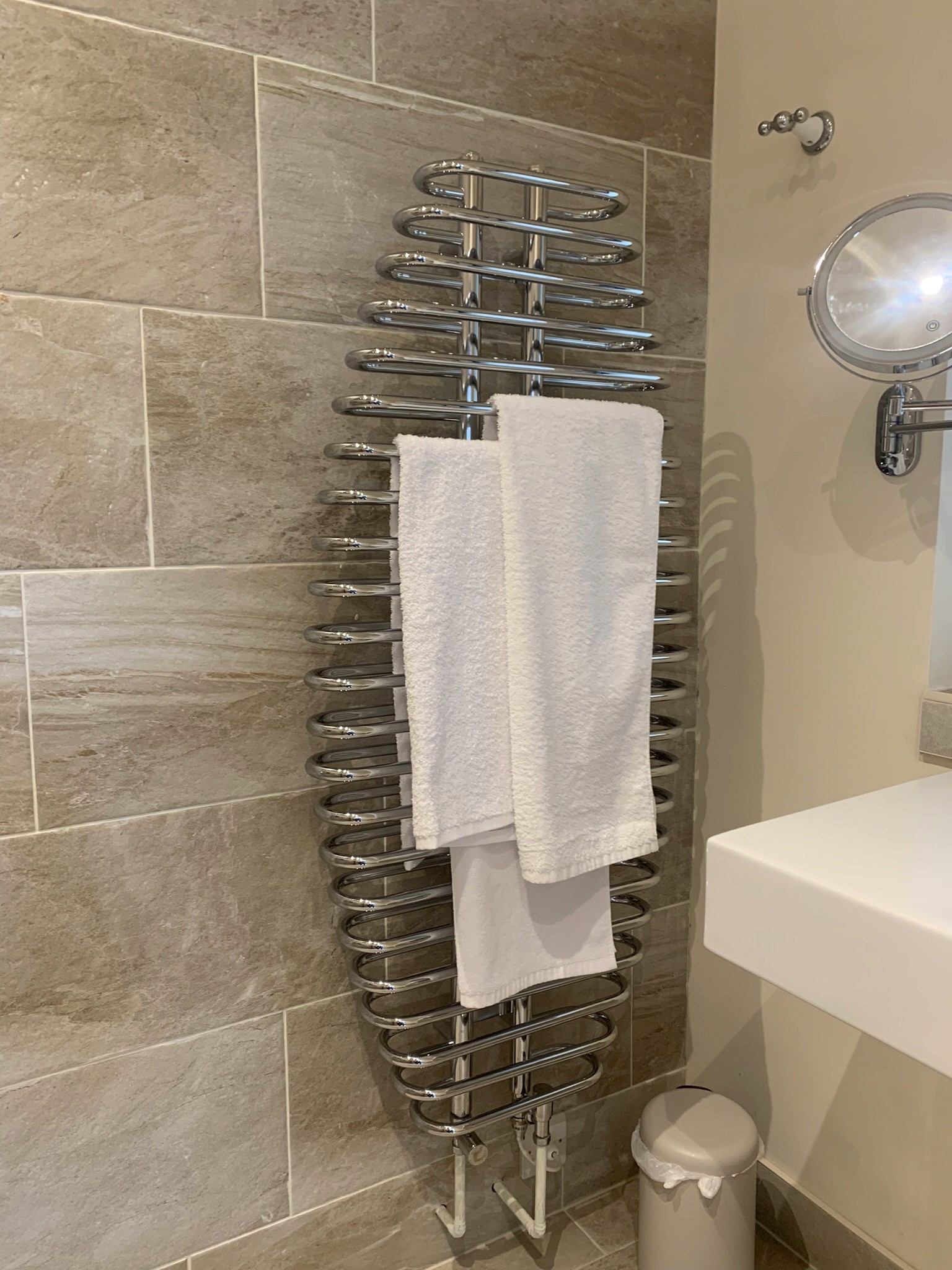 Stainless steel heated towel rail on tiled wall with white towels