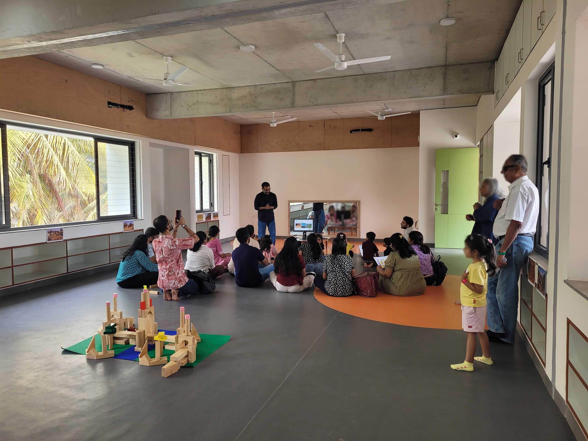 A person stands in a room with an orange-lit wall, casting a dramatic glow. Their contemplative pose is reflected on a glossy floor, evoking a serene mood