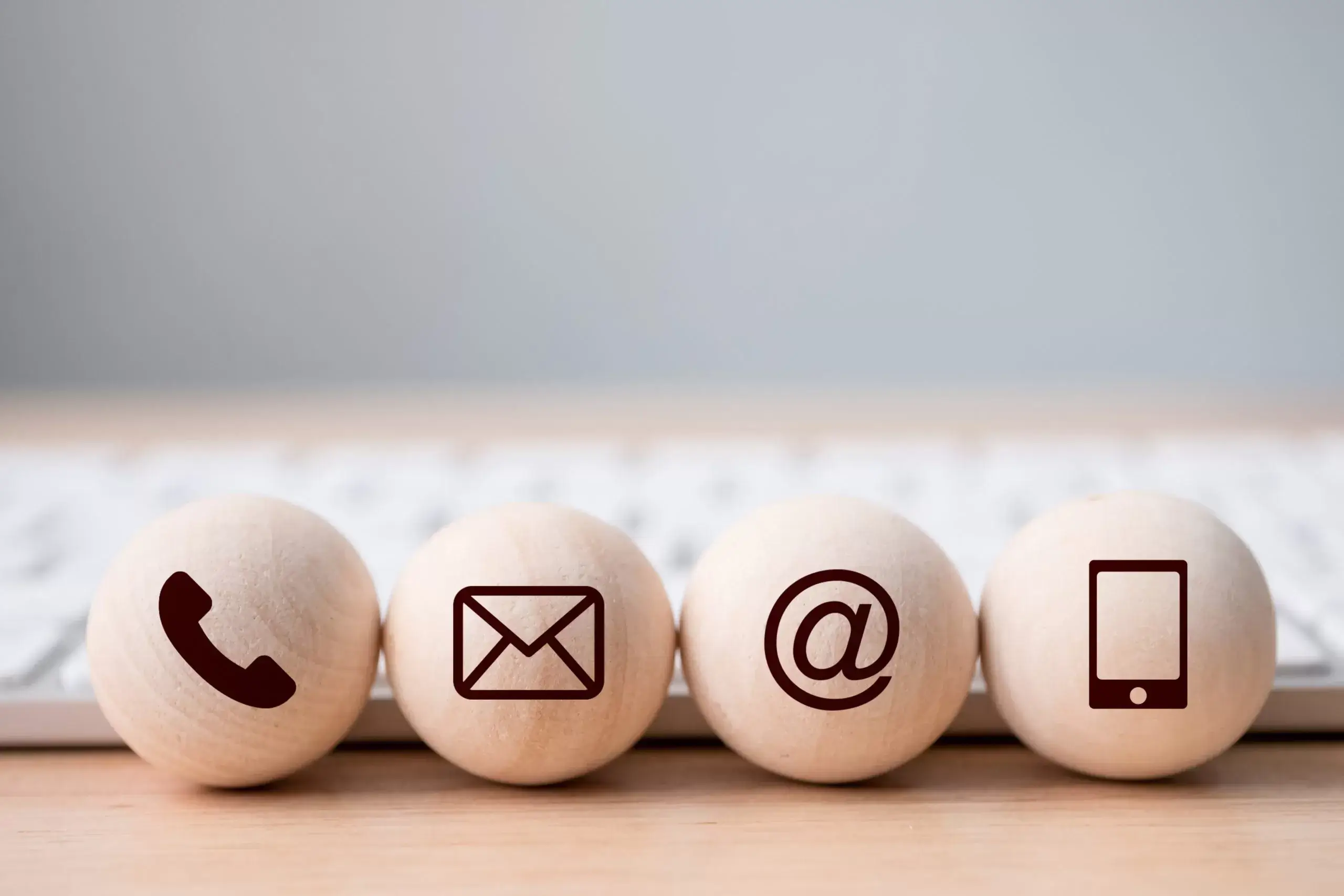 Image of 4 wood balls on a desk, each has a different symbol on - phone, mail, ampersand and mobile phone