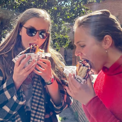Duas mulheres comendo sanduíches na rua