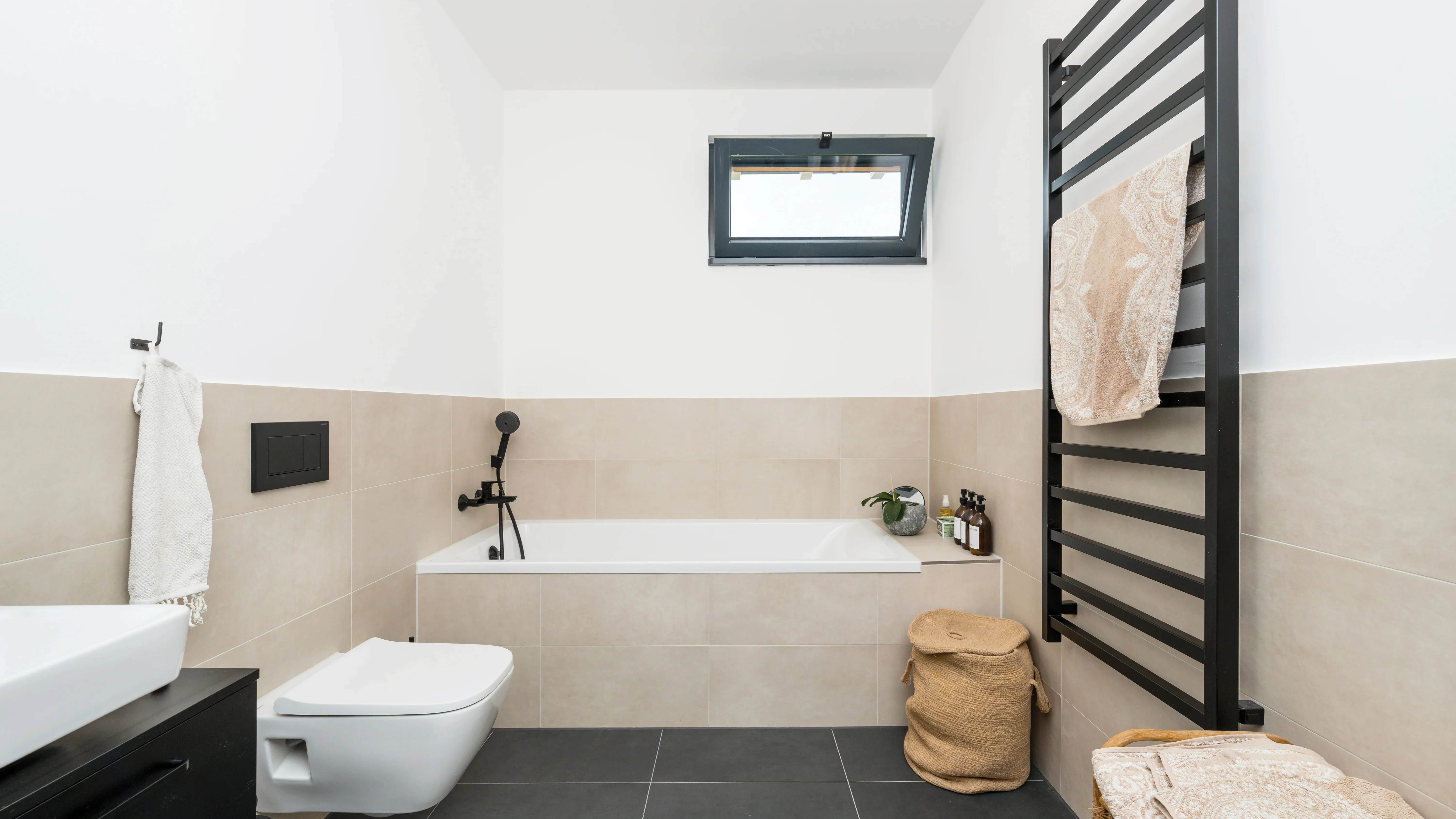 Modernes Badezimmer mit kleinem Fenster, Handtuchhalter, Badewanne, Toilette und Waschbecken.