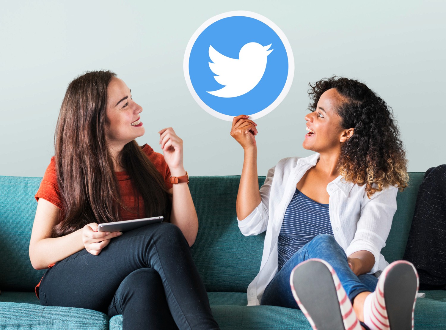  Two women seated on a couch, engaging in conversation, with a Twitter logo prominently displayed nearby.