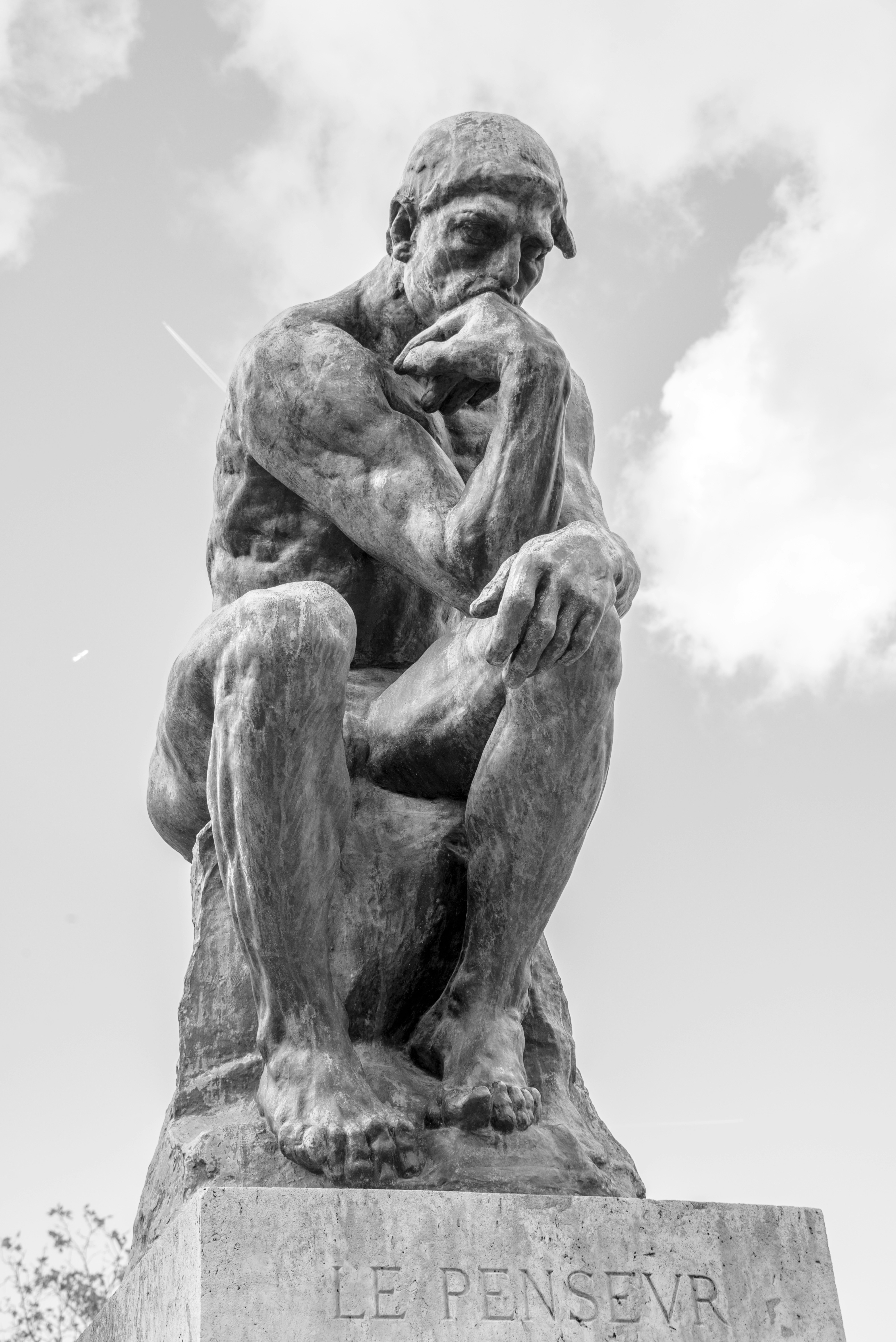The thinker statue sits outdoors under a cloudy sky.