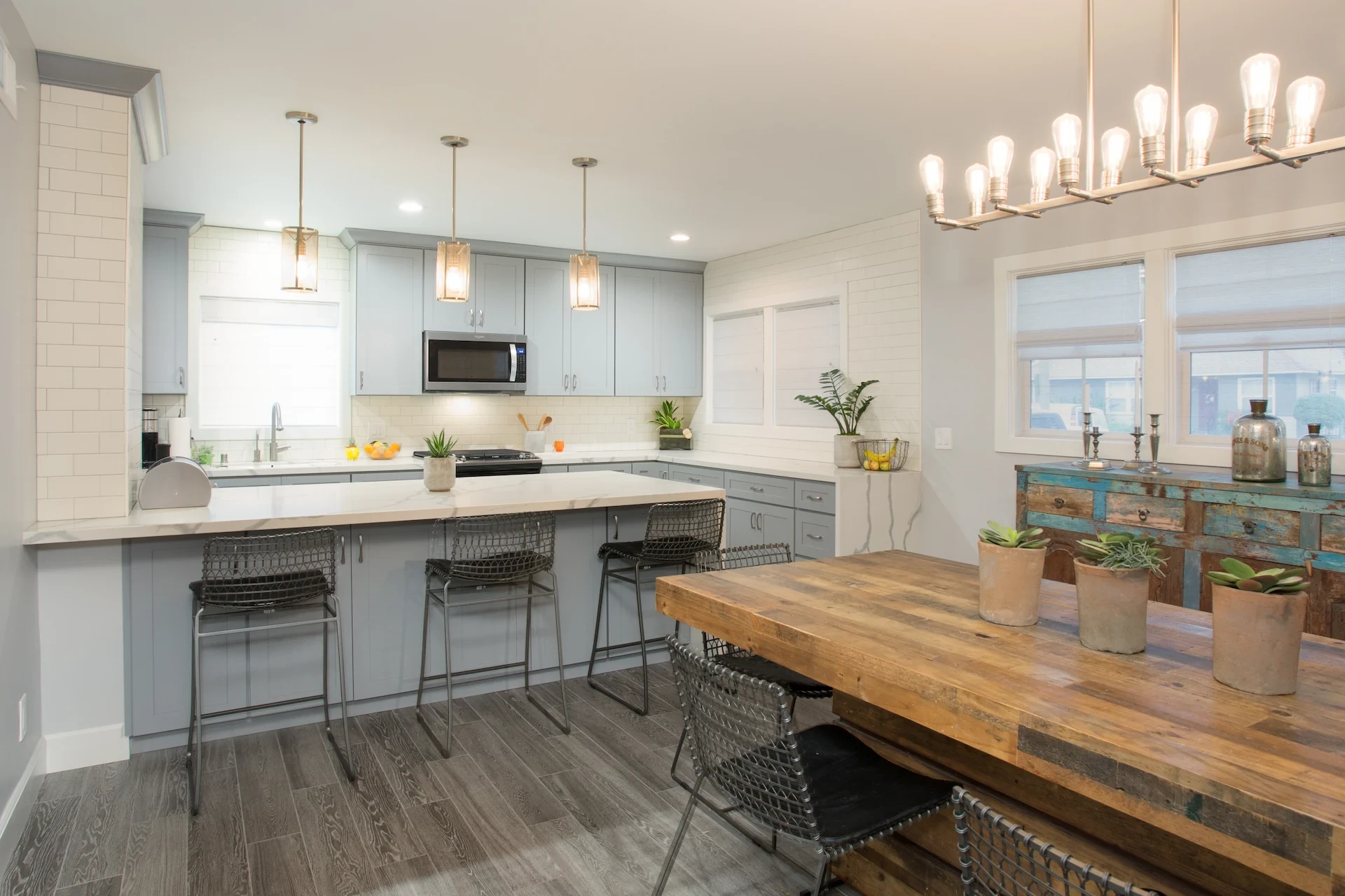 Rustic farmhouse dining room with kitchen in background. Grey floors and blue cabinetry. Photo by Chris Darnall.