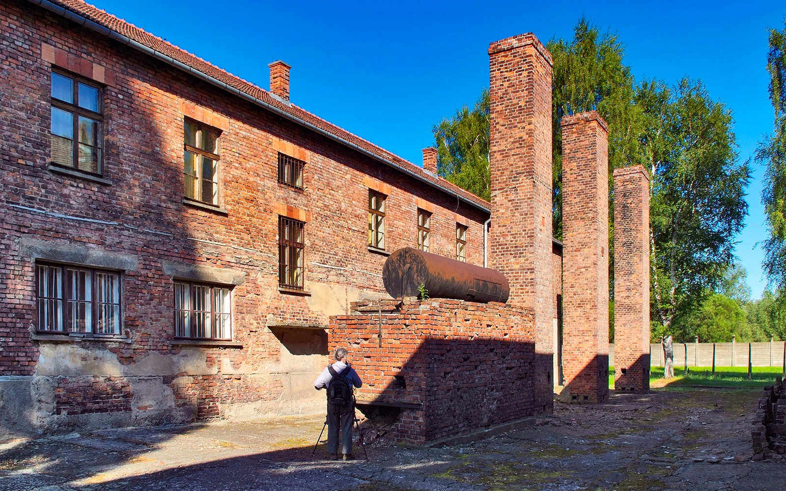 Barakkabygging og skorsteinar við Auschwitz Birkenau í Póllandi, með gesti að taka myndir.