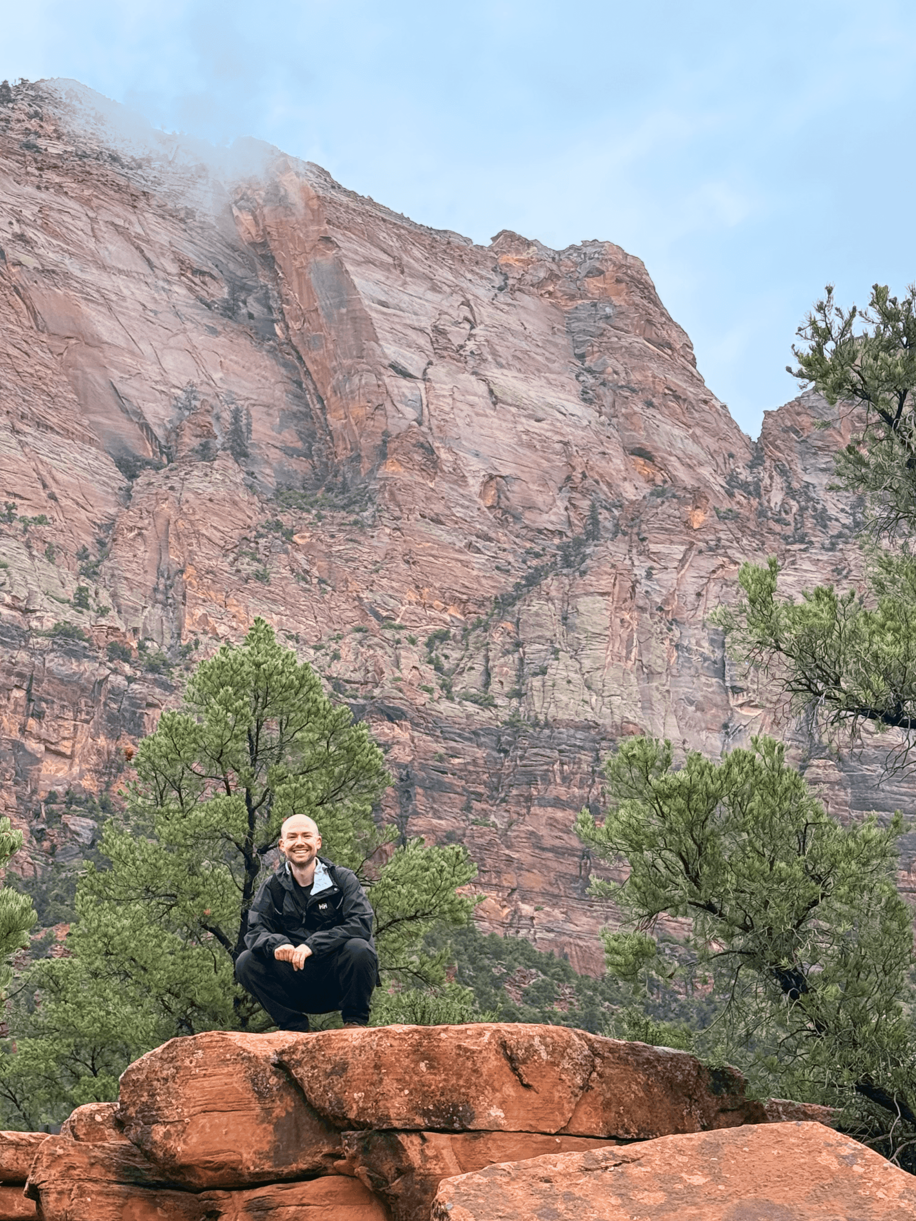 man squatting on a rock formation in the mountains