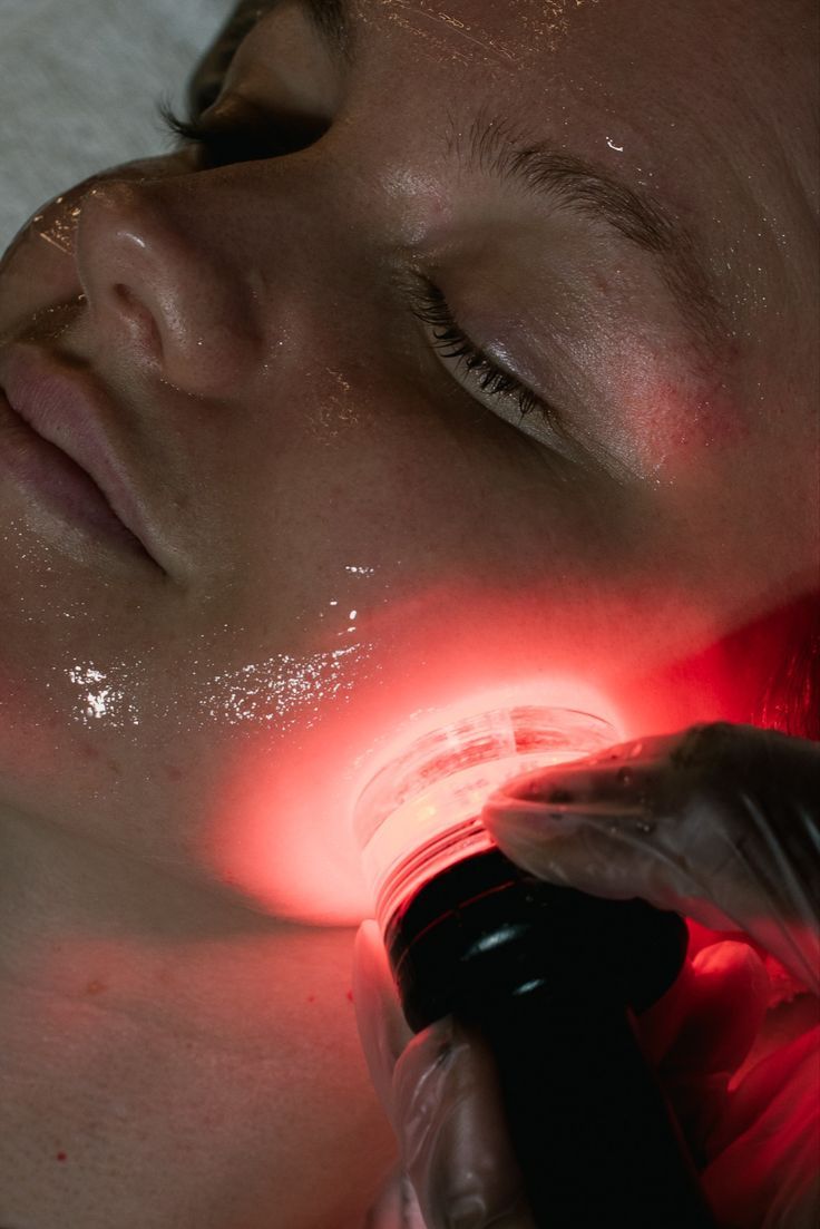 A woman lying down with a towel wrapped around her head, her face glowing with facial oil. She has a peaceful expression, enjoying a skincare treatment.
