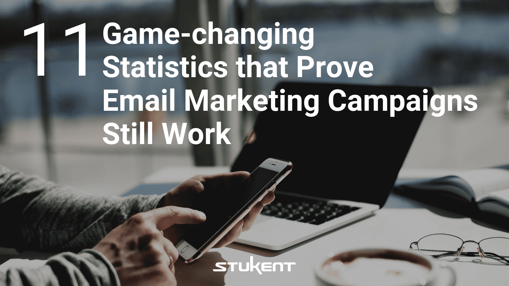 Person holding a smartphone and typing on a laptop with a coffee cup nearby; overlaid text reads: "11 Game-changing Statistics that Prove Email Marketing Campaigns Still Work" with the Stukent logo at the bottom.