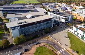 person in orange jacket standing on brown rock near snow covered mountain during daytime
