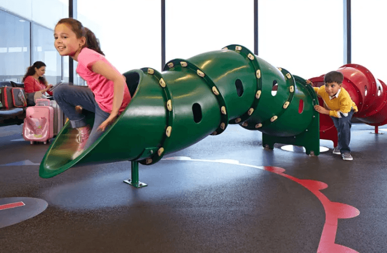 機場候機室室內兒童遊樂場設施，綠色圓筒形滑梯連安全防撞地墊。