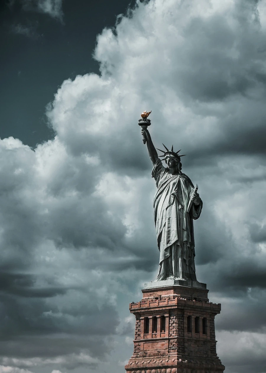 Statue of Liberty on Liberty Island in New York City, standing against dramatic cloudy skies.