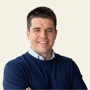 Headshot of Mark Burazin, smiling in a navy sweater over a light blue collared shirt.