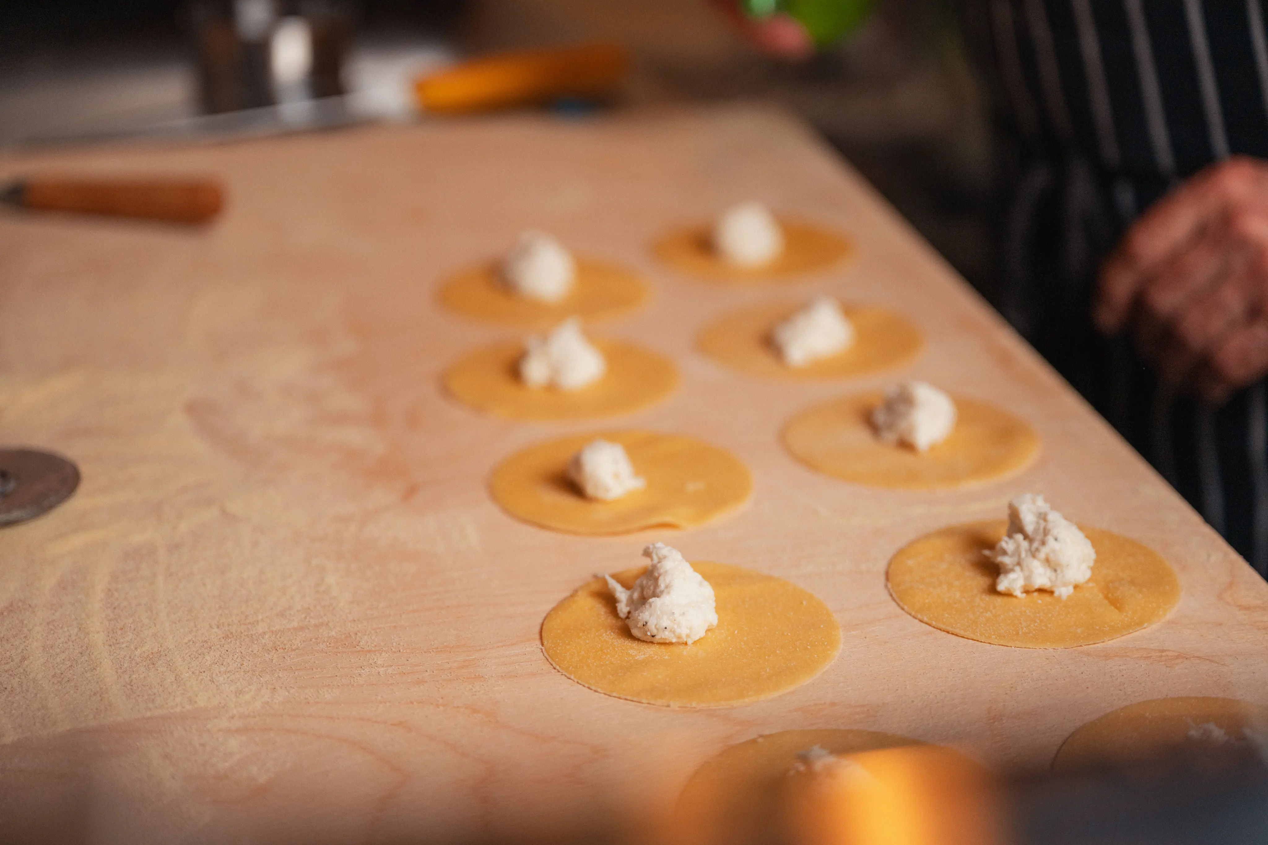 Handmade pasta being prepared on a wooden surface with dollops of filling on circular dough pieces, capturing the artisanal culinary process in an Italian restaurant in Piccadilly, London.