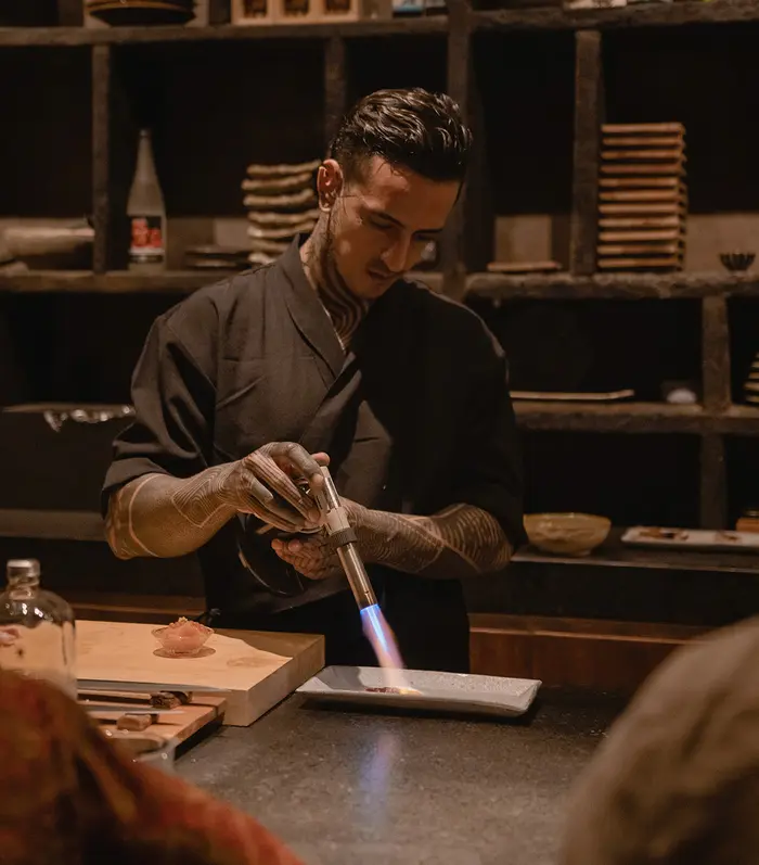 Person using a torch to heat a dish at Japanese restaurant Kuu in Nômade Tulum, Mexico.