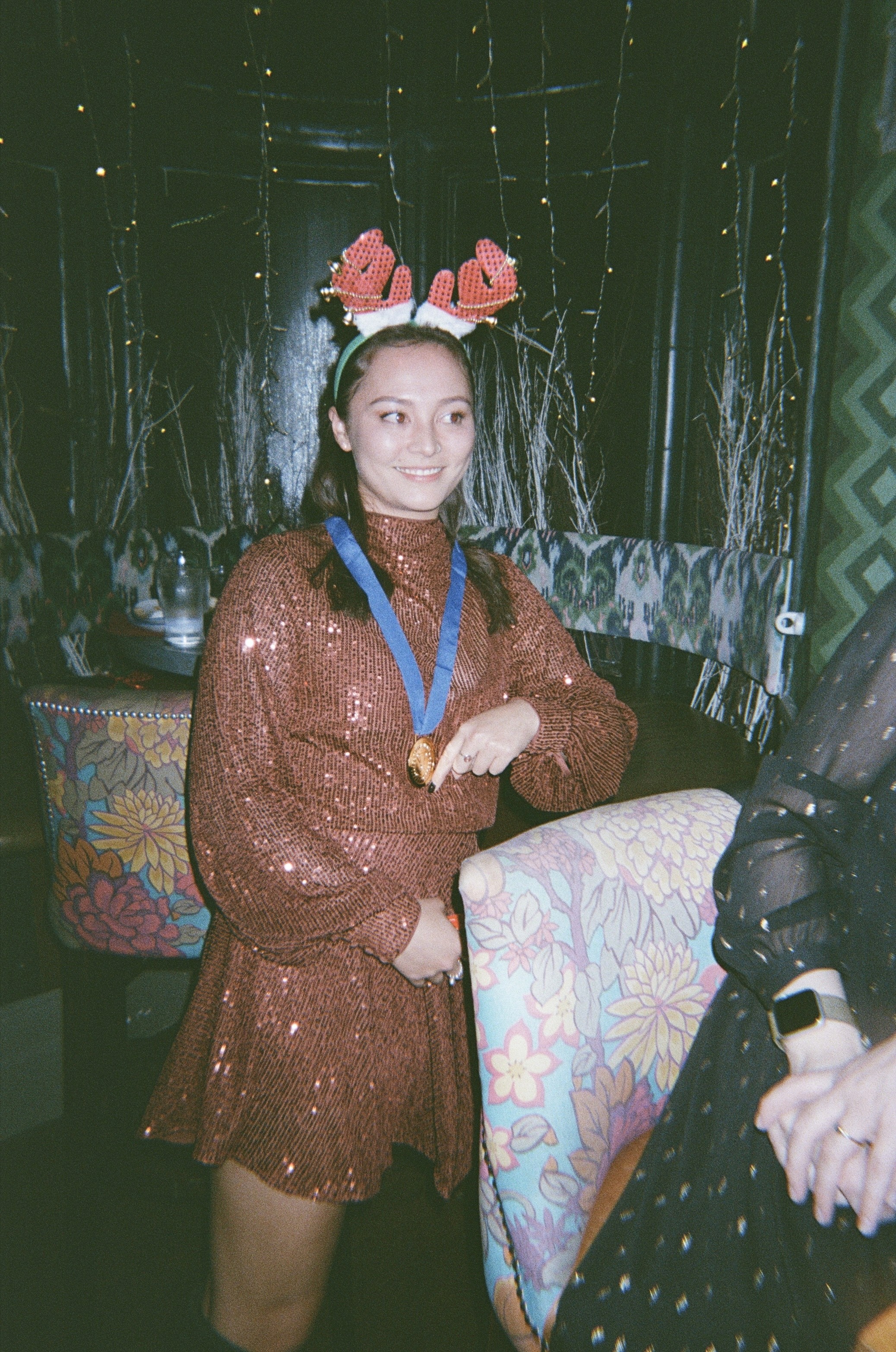 Tsui in a sparkly red long sleeved dress, wearing reindeer antlers and holder her medal for winning the 'Little Miss Sunshine' award