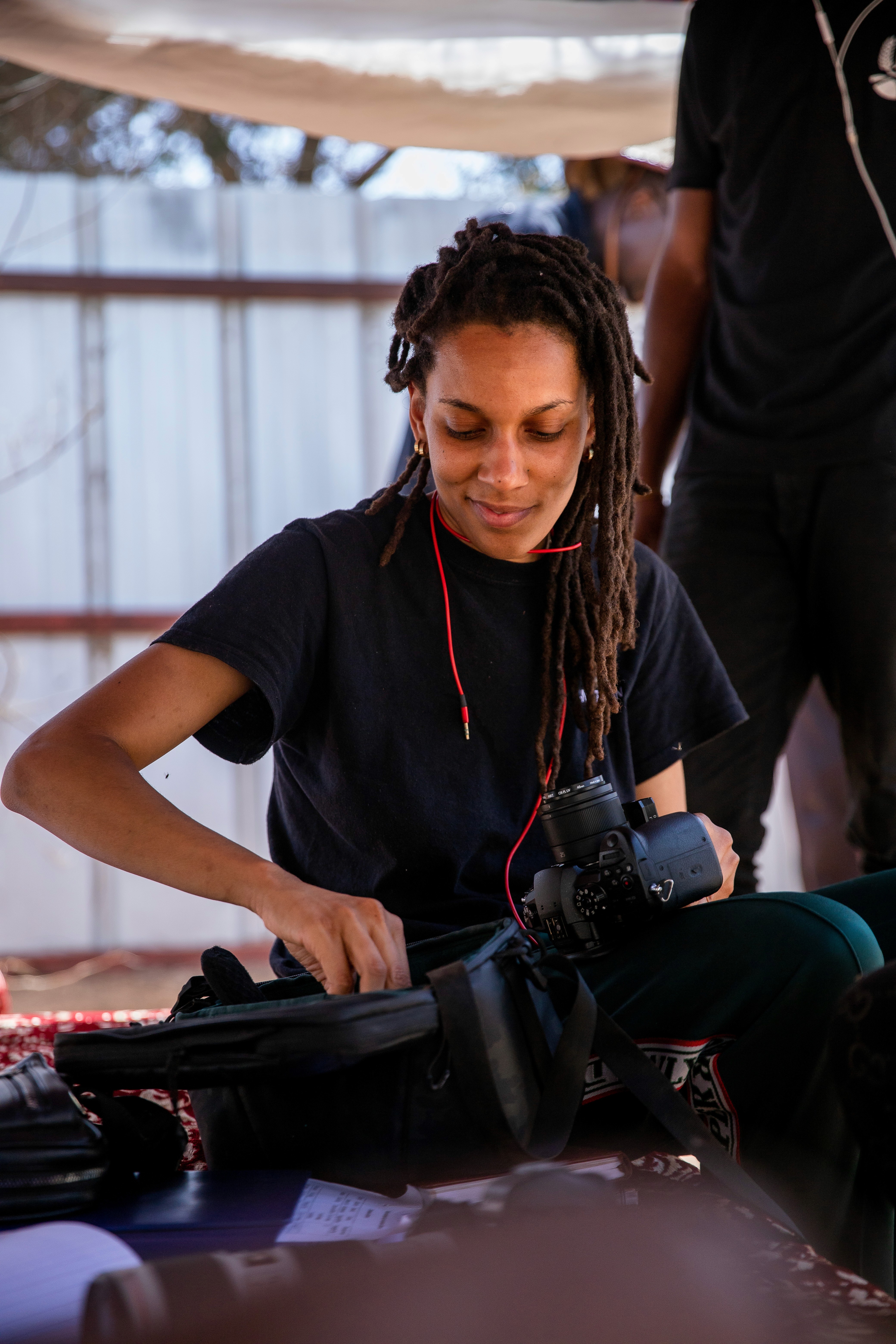 A young person in silver sports sunglasses, a white shirt, and a black sweater sits on the floor, holding an open book and leaning against a teal couch.