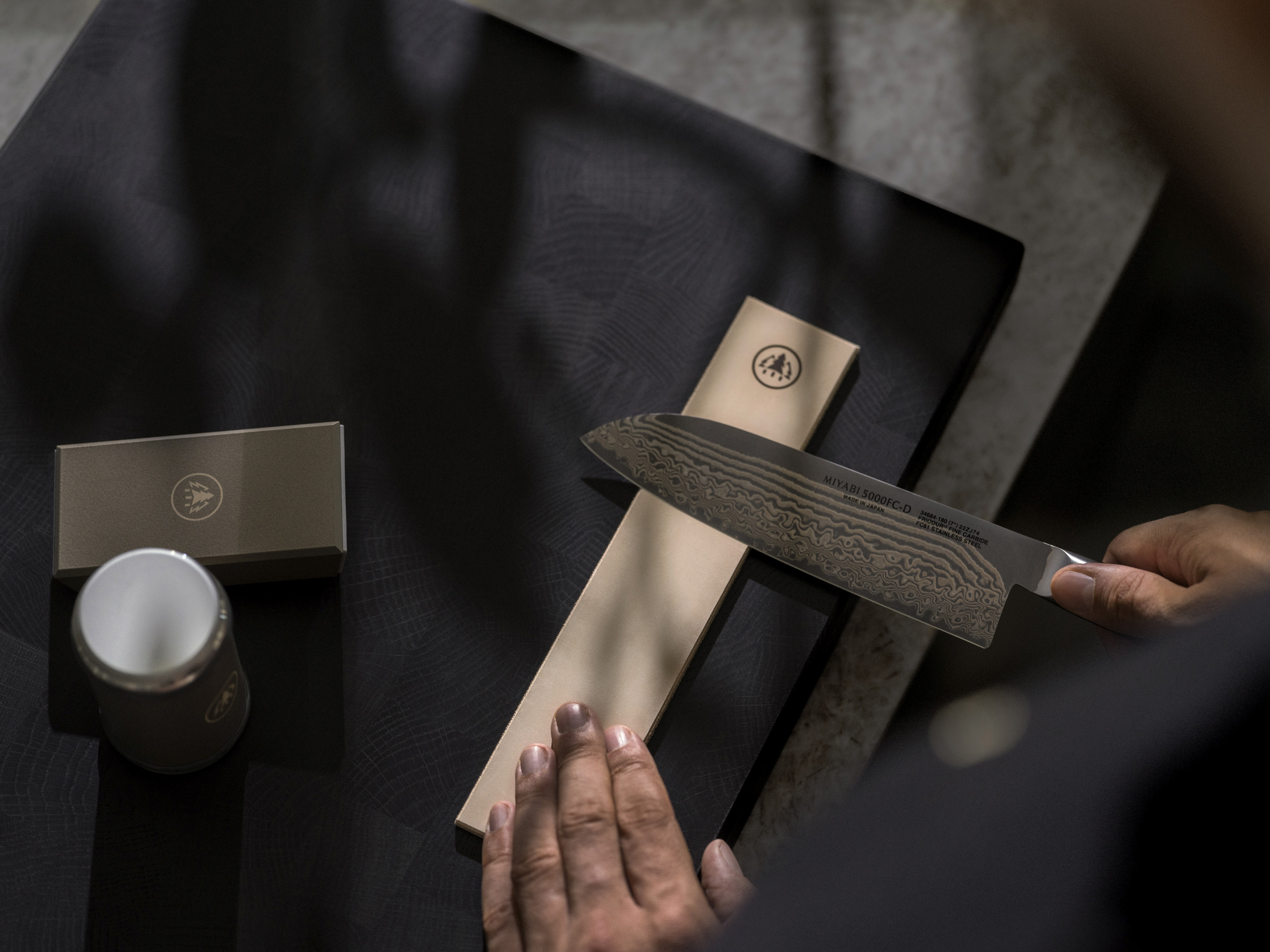 Eine Hand beim präzisen Abziehen eines Damastmessers auf einem Streichriemen aus Leder für eine polierte, rasiermesserscharfe Wate.