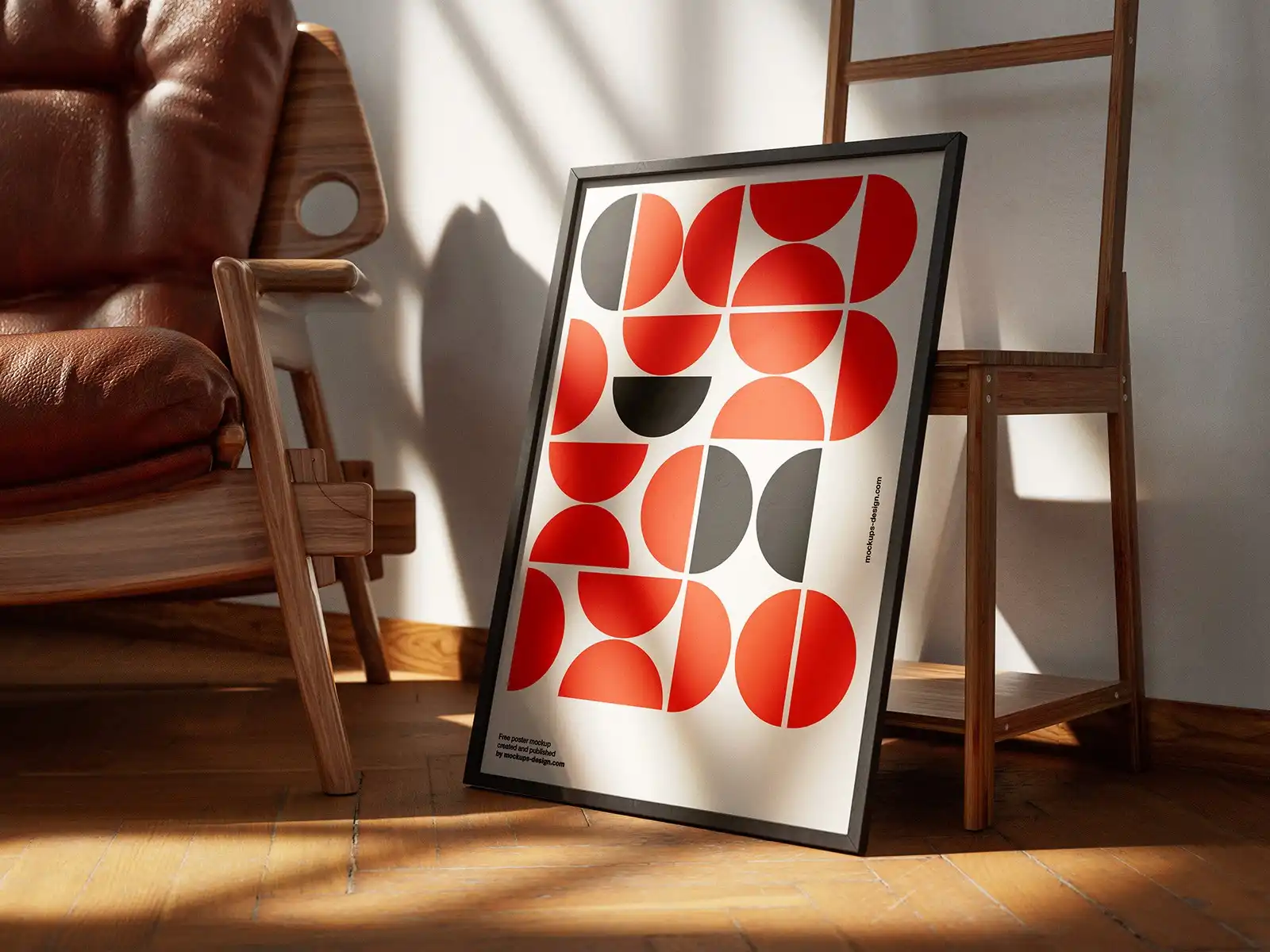 Framed poster mockup leaning against a wooden chair, featuring bold geometric patterns in red, black, and white. Set in a cozy interior with warm natural lighting and wooden flooring.