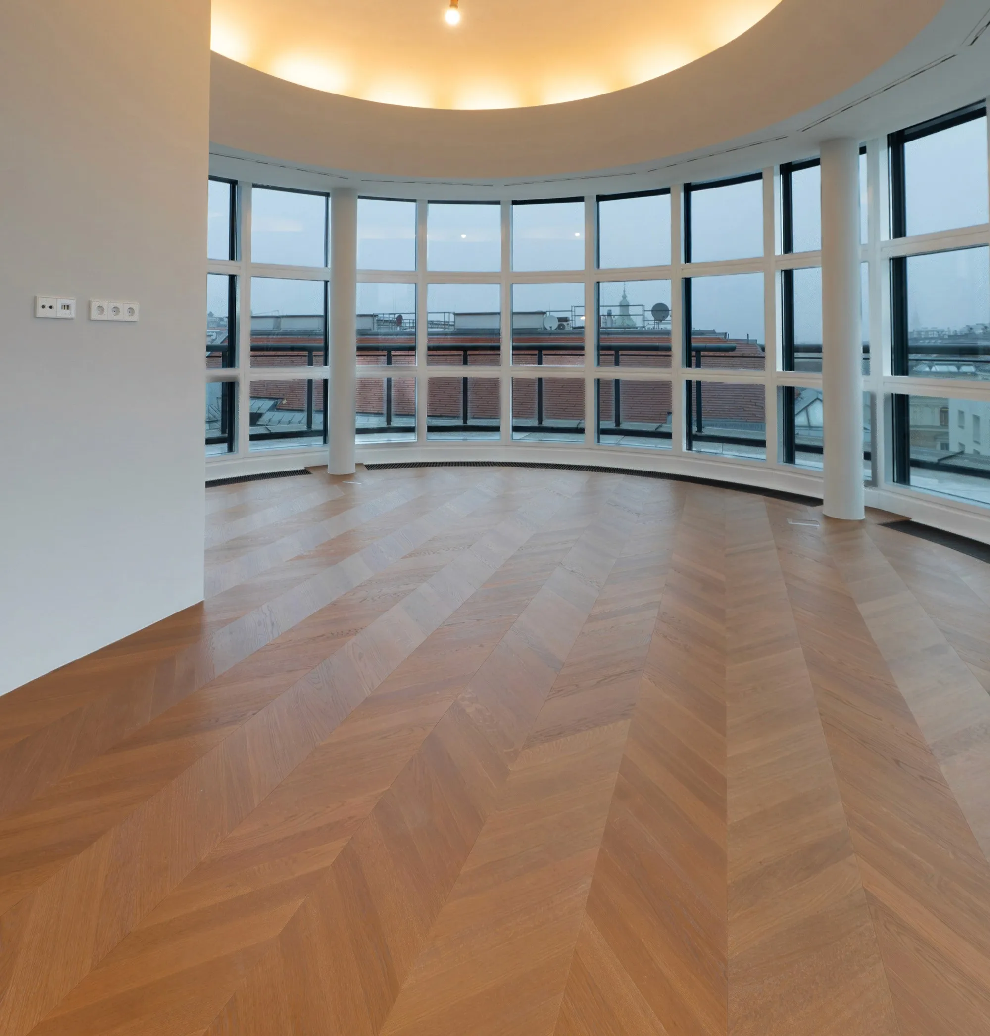 Großer Wohnraum mit gebogener Fensterfront und hochwertigem Chevron-Parkettboden.