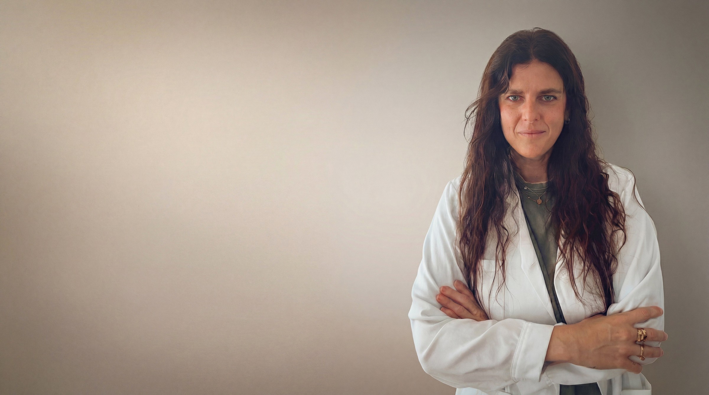 Smiling female doctor in a white lab coat, standing against a neutral gray background, exuding professionalism and approachability.
