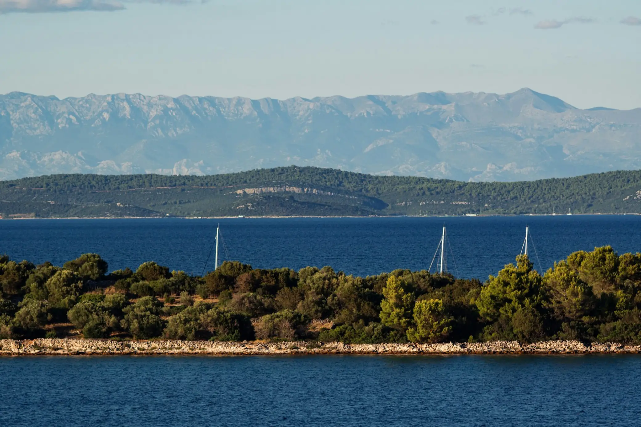 Voiliers sur une mer Adriatique calme, montagnes en arrière-plan