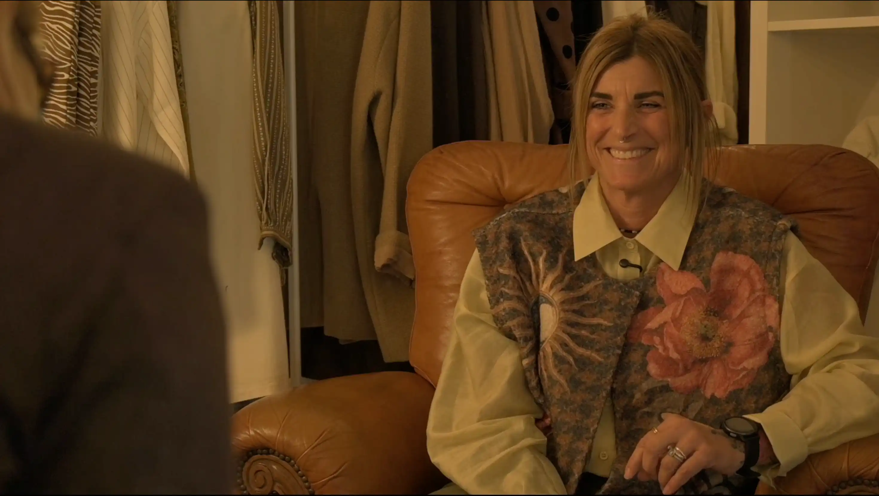 Donna ride seduta su una poltrona in pelle dentro un negozio di abbigliamento mentre viene intervistata per il documentario donne in bilico