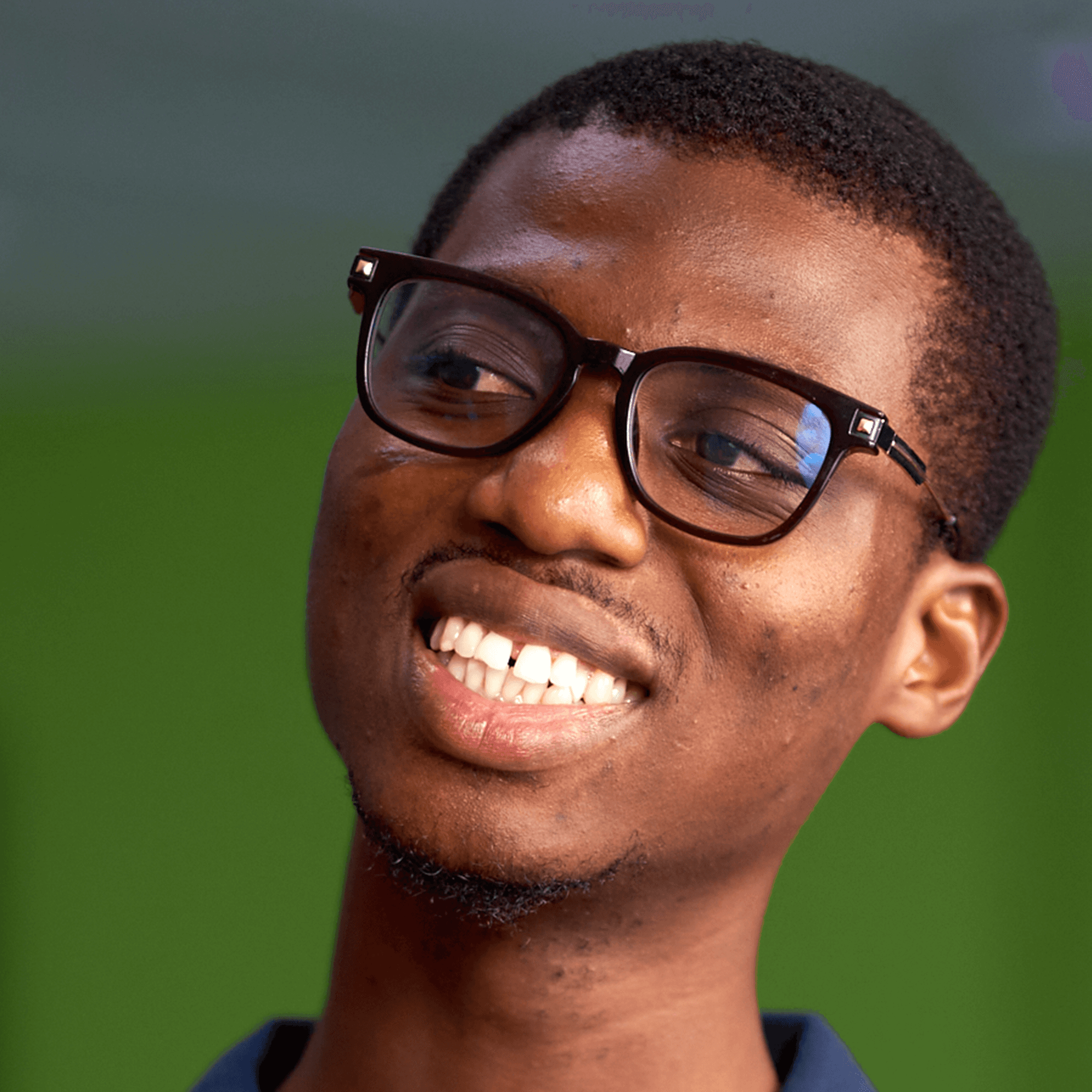 Young man with glasses smiling against a green outdoor background.