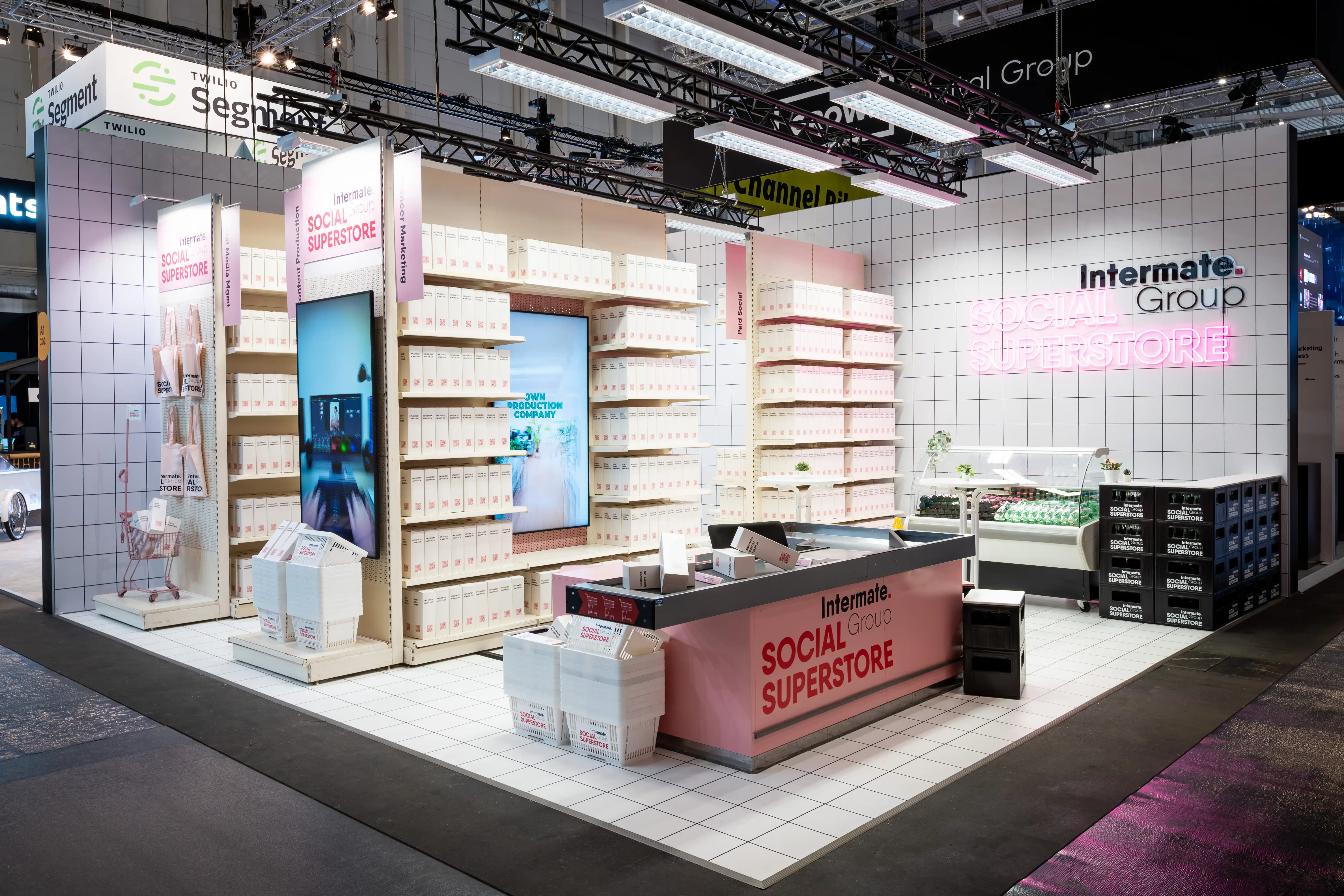 The Intermate Social Superstore booth at OMR staged as a supermarket with shelves, checkout and neon lettering on tiled walls.