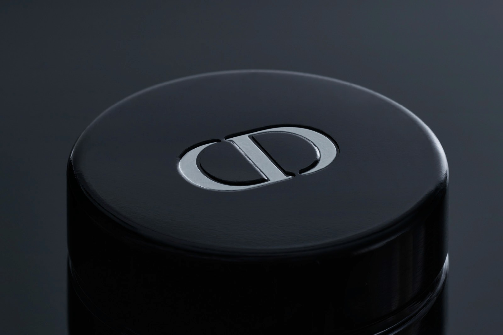 Close-up of a sleek black cylindrical object featuring a minimalist Christian Dior logo on its top surface.