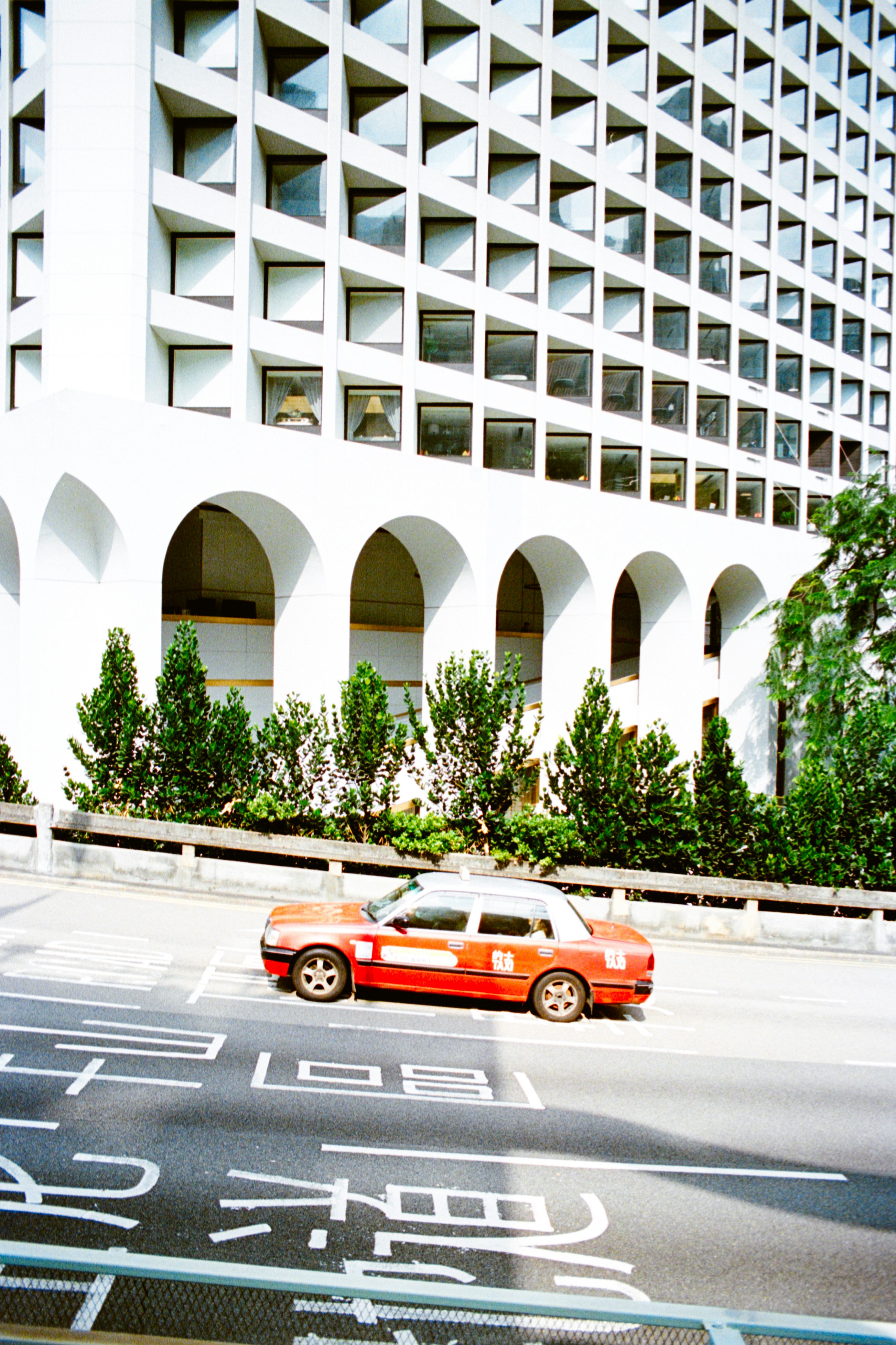 Red and white taxi drives past modern building arches.