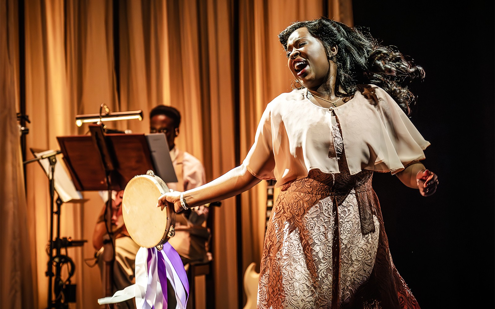 Performer singing and playing tambourine in Marie & Rosetta production.