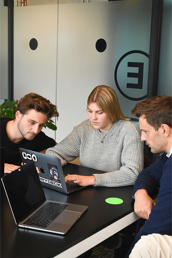 Three people sititng around two laptops in an office space in a training session