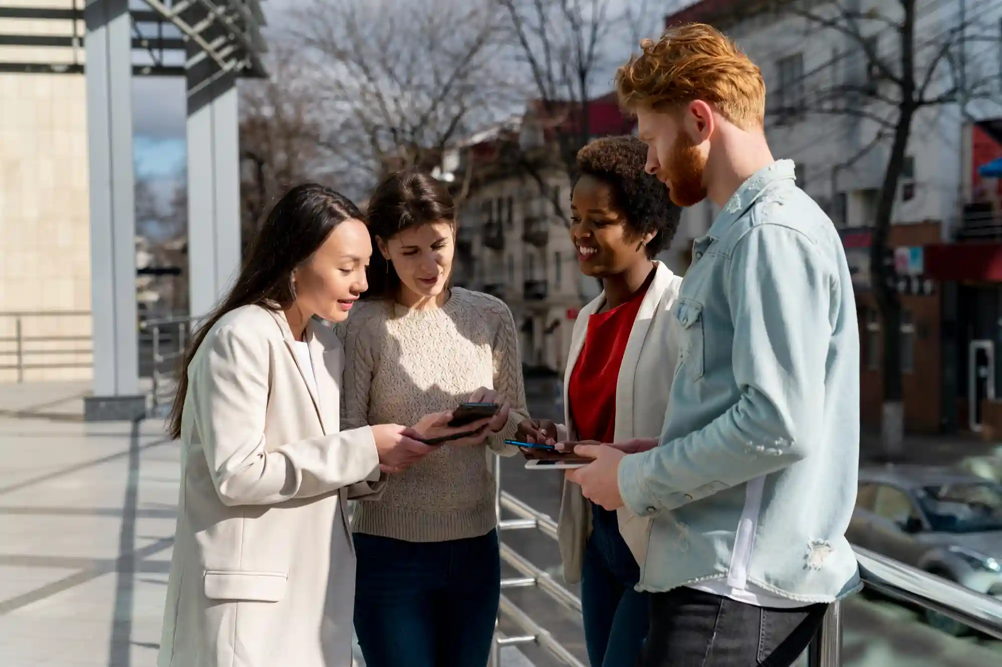 A diverse group of colleagues standing outside, collaborating and sharing information on their smartphones.