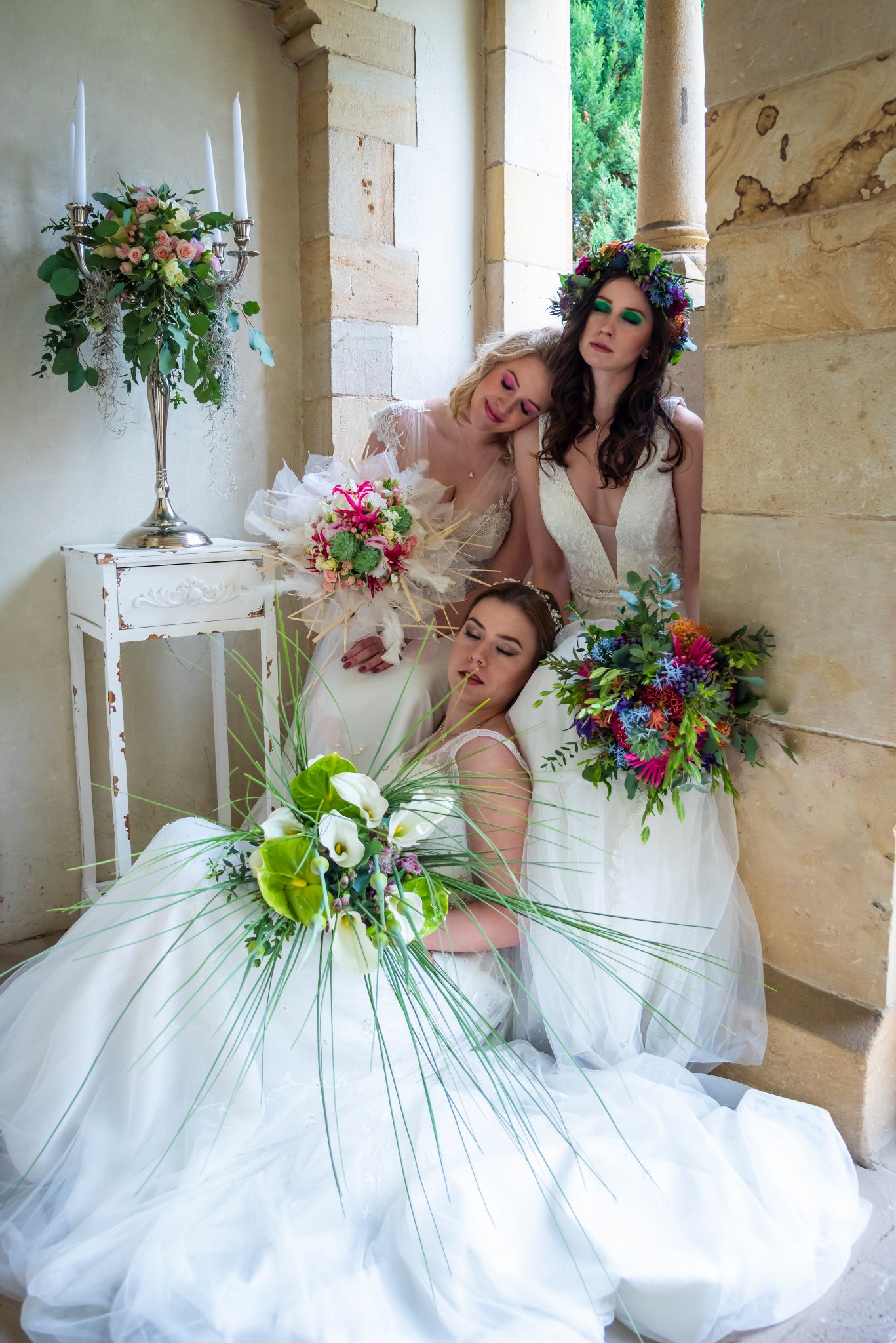 Drei Bräute posieren zusammen in Winterhochzeitskleidern und halten ihre Brautsträuße aus Edelweiß, Amaryllis und Tannenzweigen.