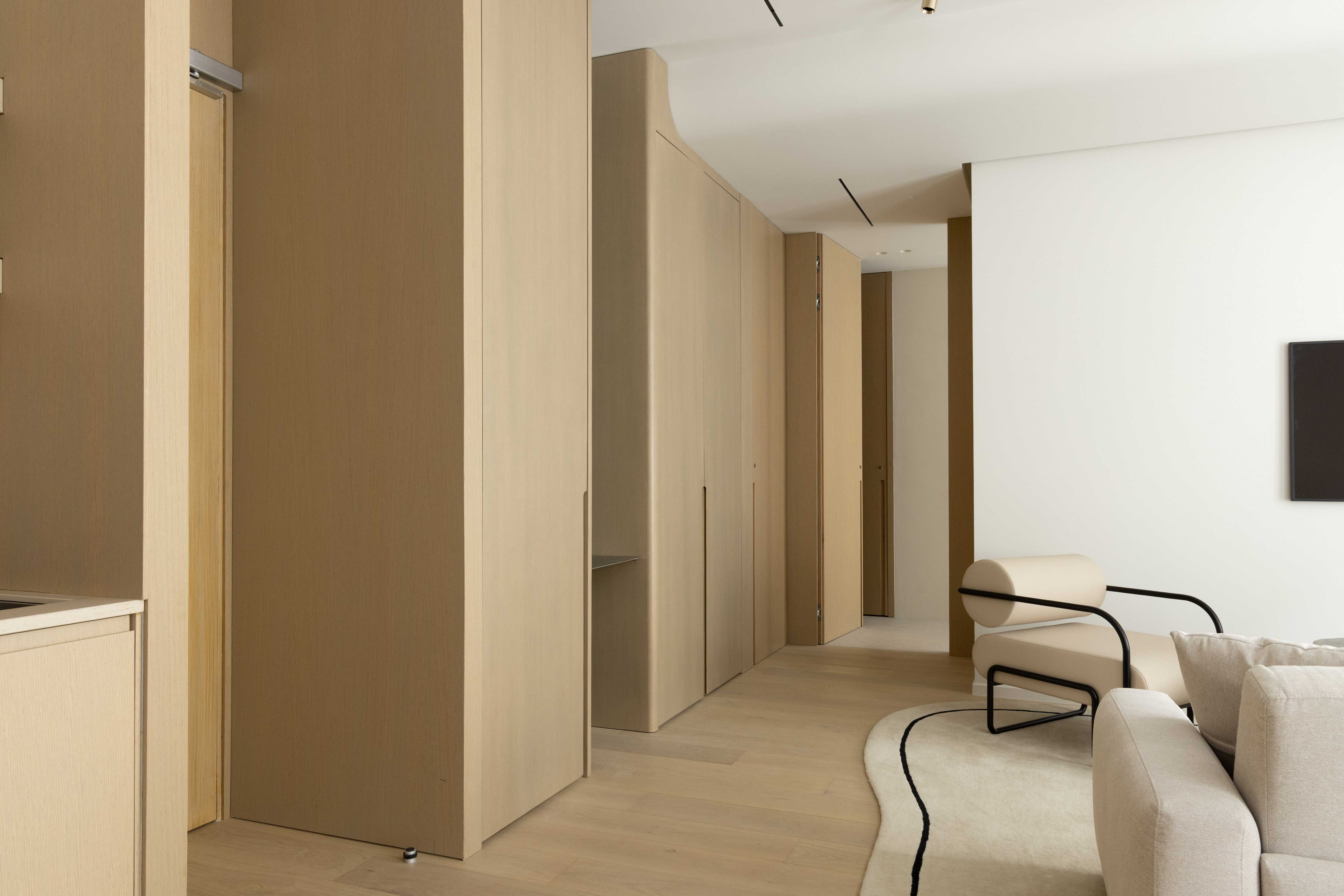 Couloir de l'appartement avec placards integres en bois clair, parquet et fauteuil design beige en arriere-plan