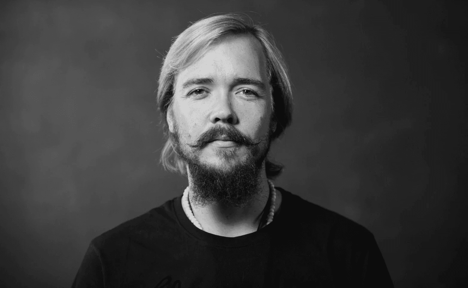 Retrato en blanco y negro de hombre con pelo rubio de longitud media y camisa negra