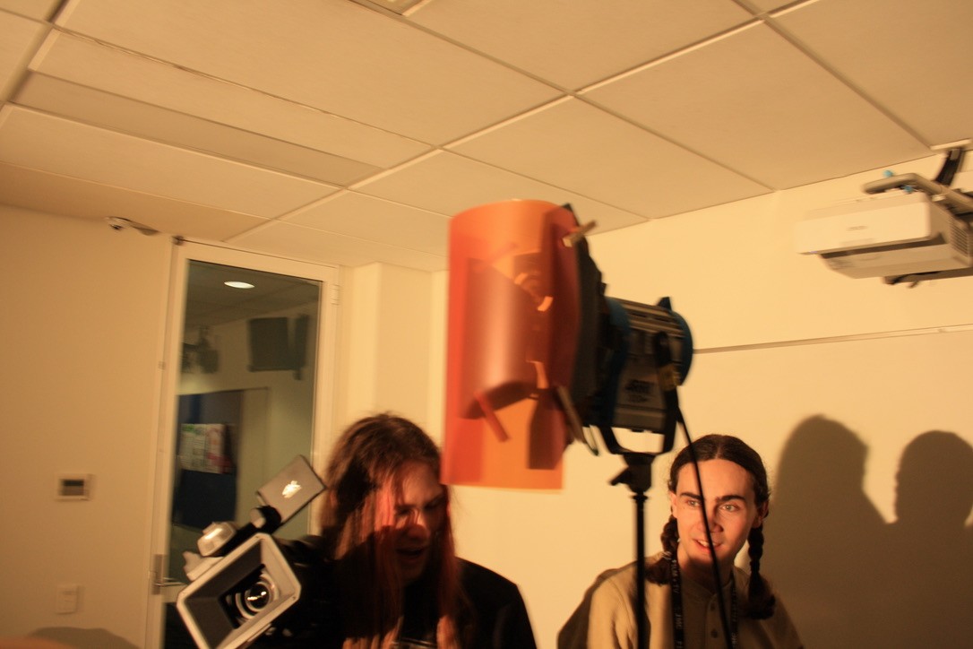 Two people standing in front of a projector screen and a 650W Arri light with a red gel.