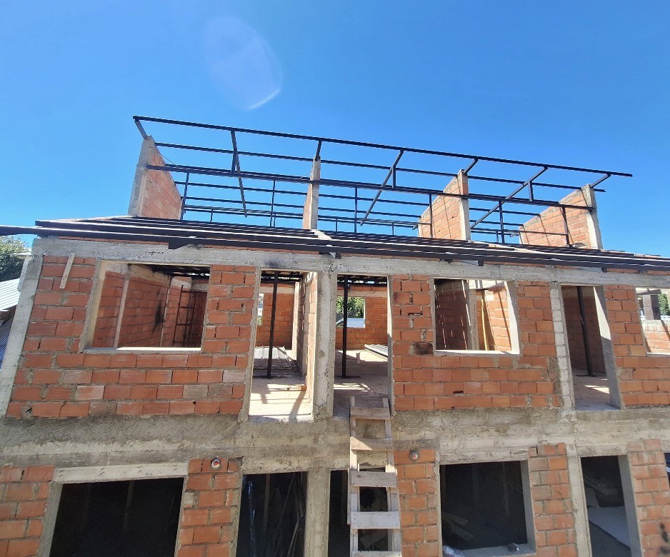 Modern two-story home with large glass windows, warmly lit interiors, and a balcony. Surrounded by trees and a manicured lawn at dusk. Cozy ambiance.
