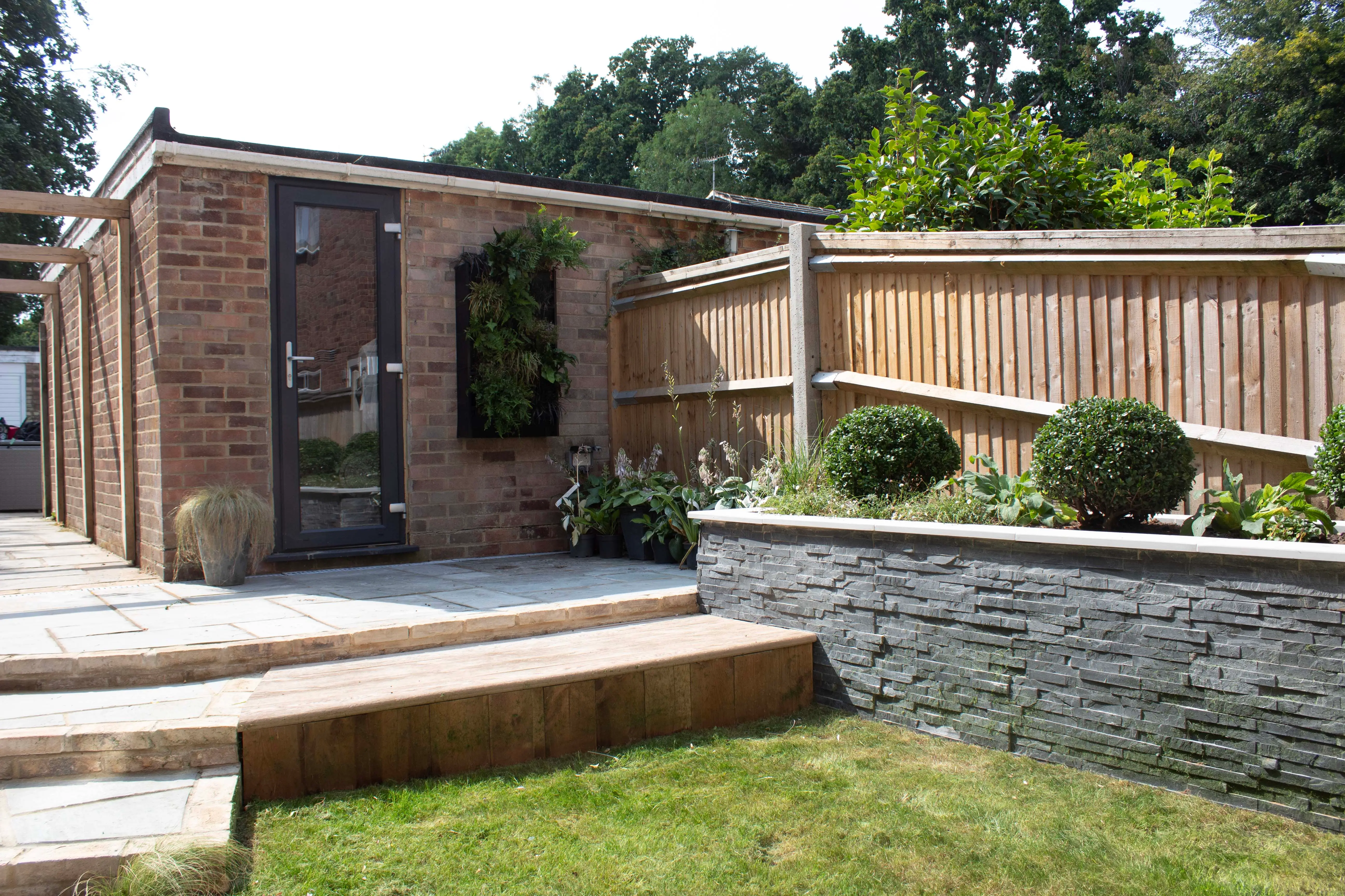 A landscaped outdoor area featuring a brick wall, wooden fence, and manicured plants with a paved pathway.