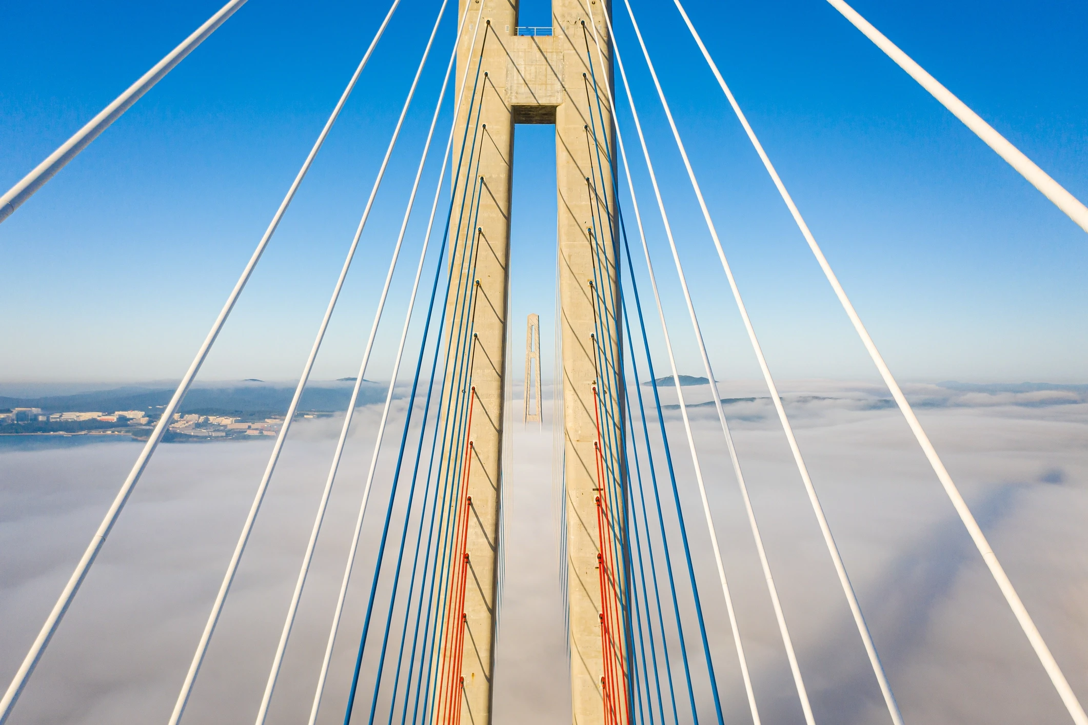 Bridge tower above clouds with cables on either side