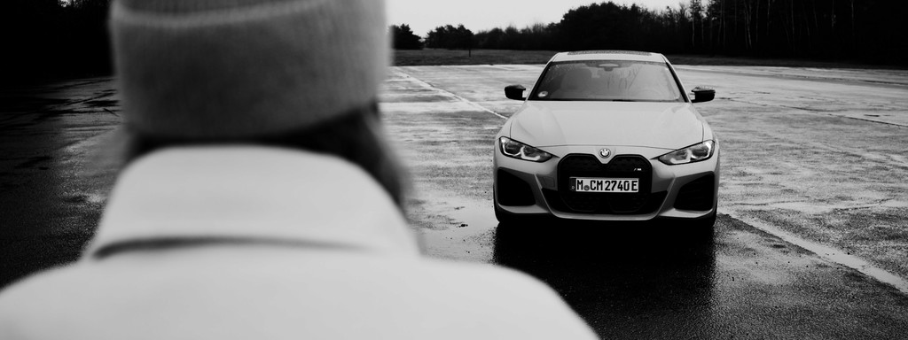 Black-and-white front view of a BMW i4 with a woman in the foreground