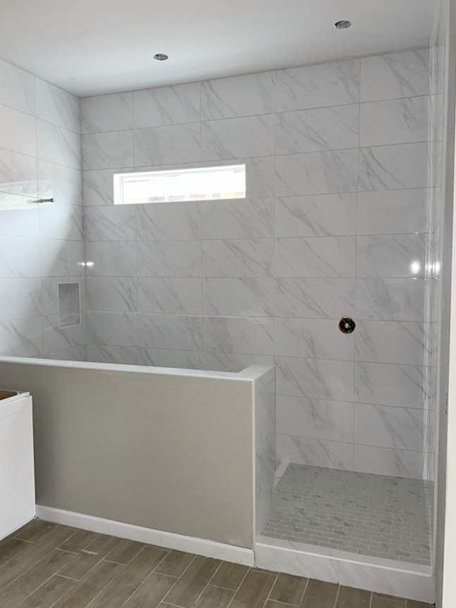 Contemporary shower with large format white marble-look wall tiles, a built-in niche, and a light grey mosaic tile shower floor.