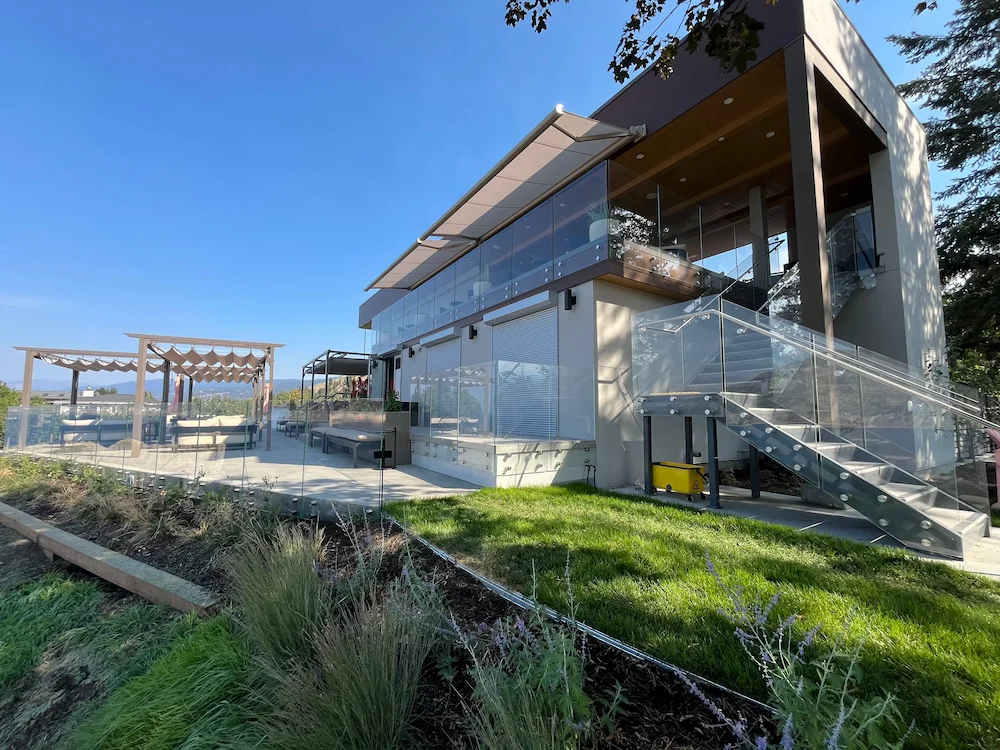 Luxury waterfront property featuring full-height glass railings along patios and exterior staircases, offering unobstructed lake views.