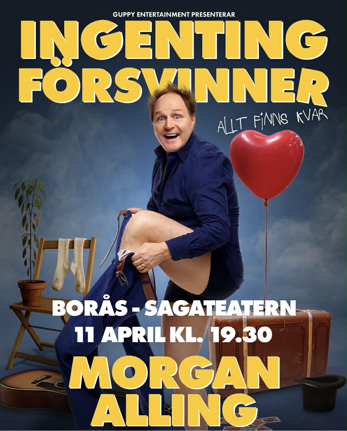 A young person with curly hair smiles at the camera while sitting in front of a laptop against a dark background.