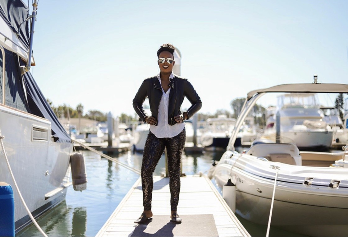 A person stands confidently on a dock surrounded by boats under a clear blue sky.