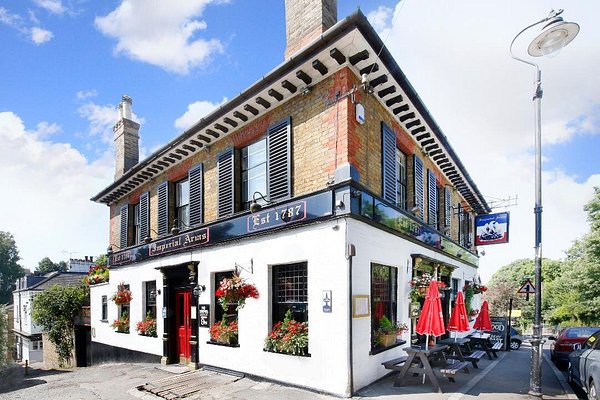 A smiling man with curly hair is sitting at a desk, looking at the camera, with a laptop and a lamp in the background.