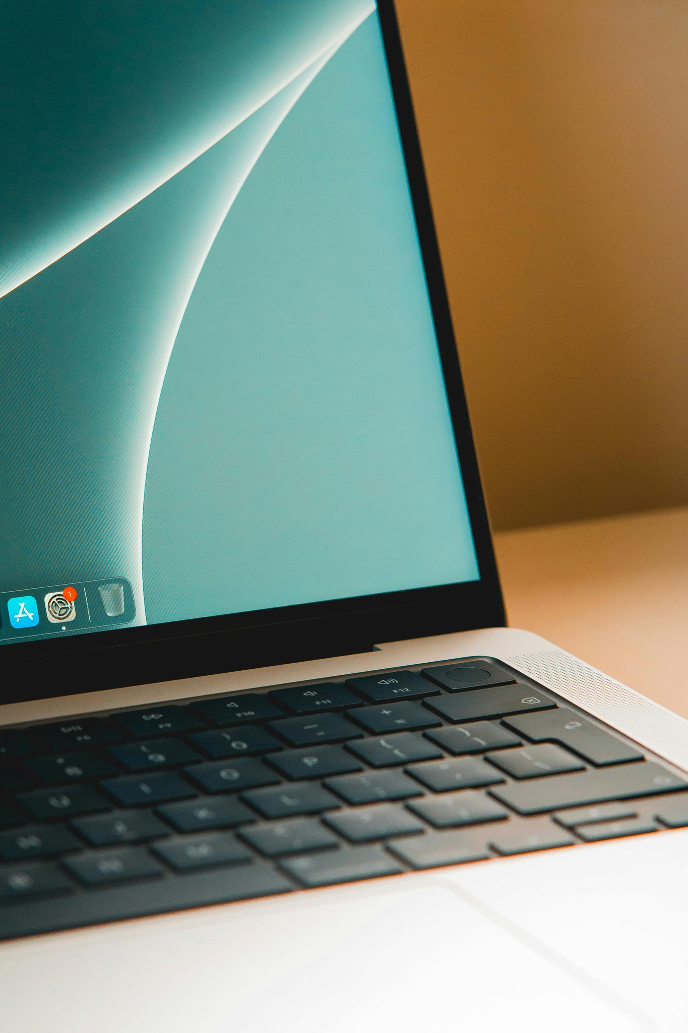 A close-up view of a laptop keyboard and screen, resting on a wooden surface with a soft light backdrop.