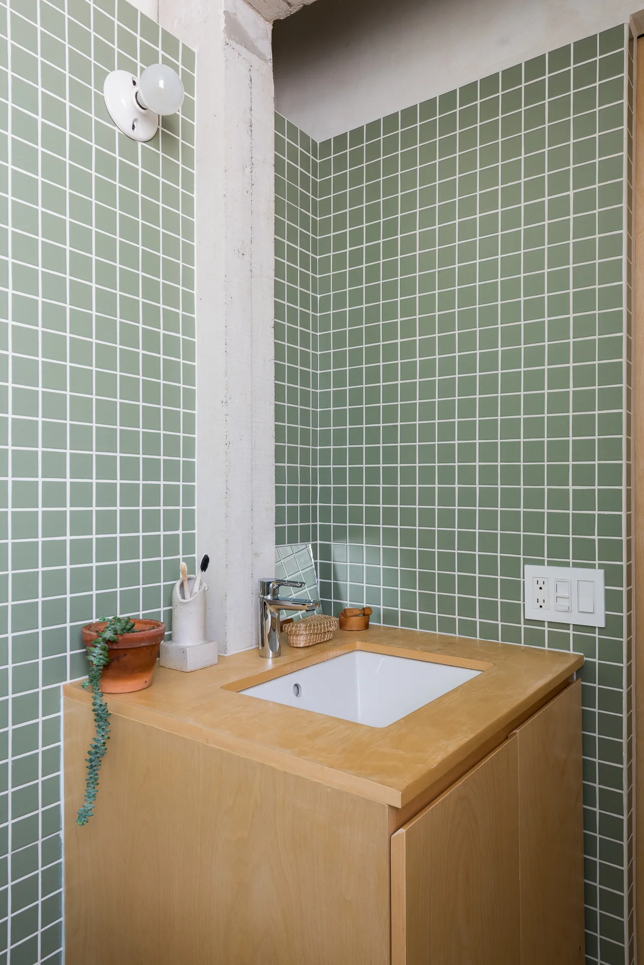 Espejo y lavabo de madera reflejando el baño de mosaico verde