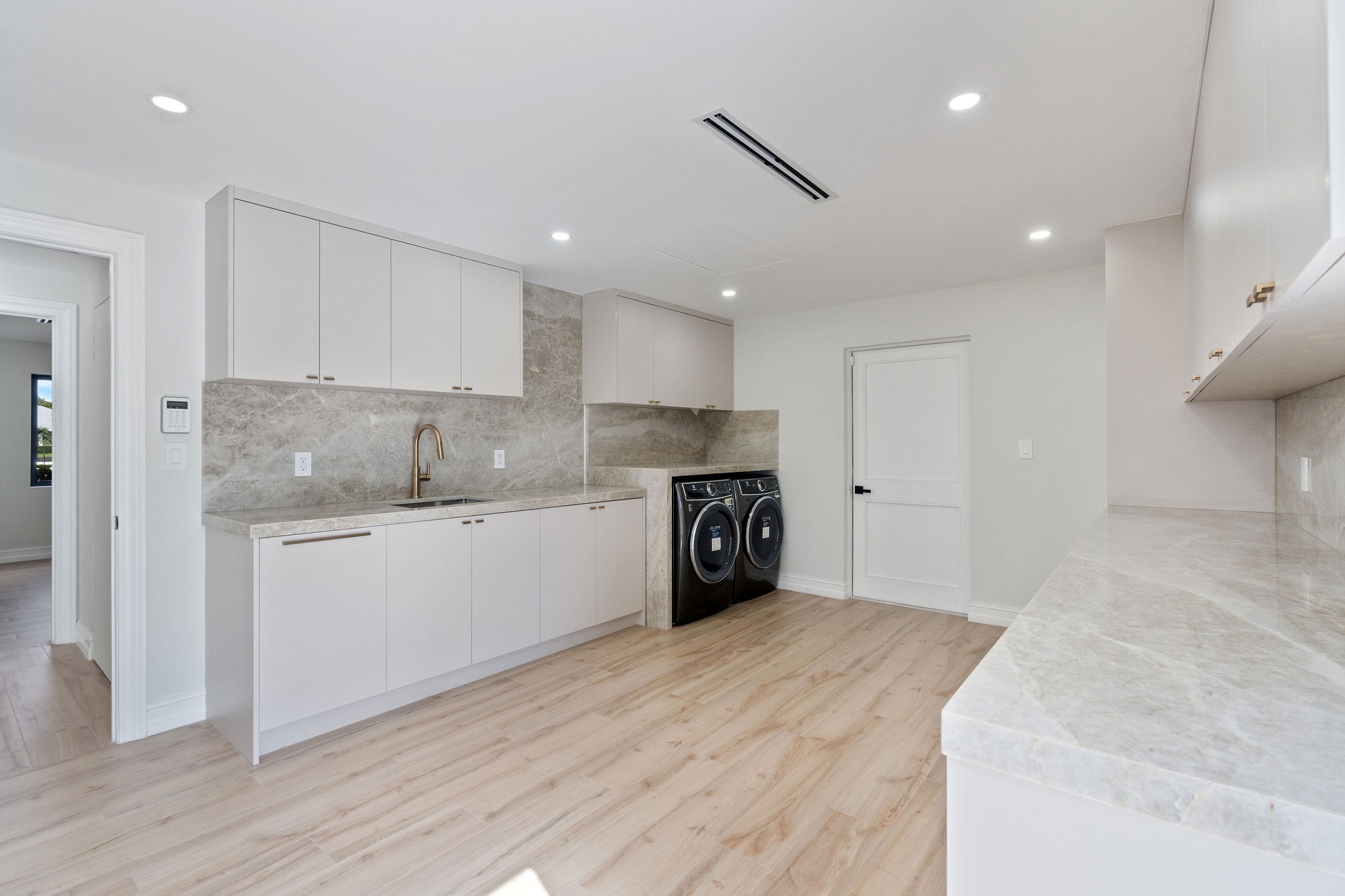 Modern laundry room with white cabinets, marble countertops, sink, and black washer/dryer.