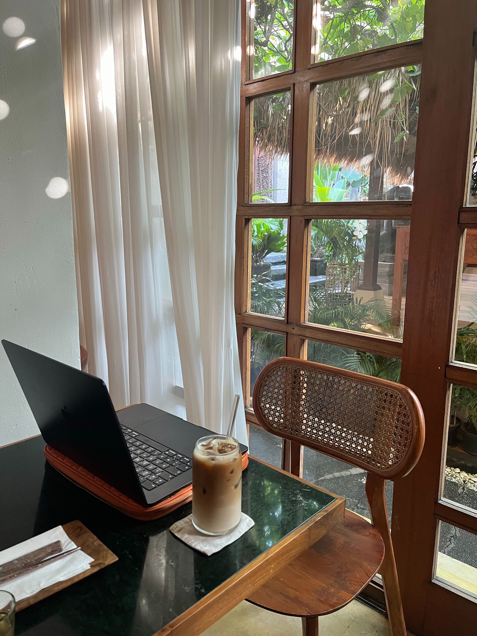 laptop on a table with a iced coffee beside it and large window behind
